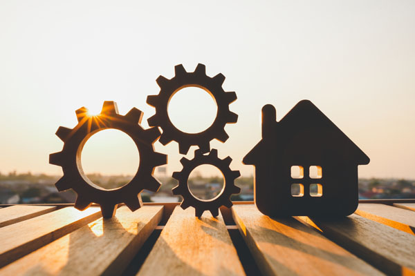 a wooden house and cogs balancing on a table with the sunset behind